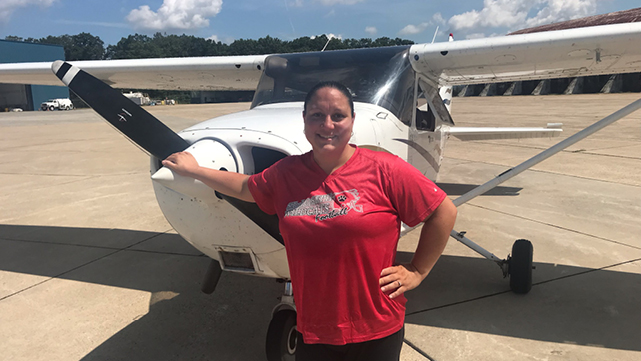 Student standing in front of an airplane on the the runway.