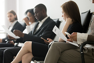 people in a waiting room dressed professional waiting for an interview reading papers