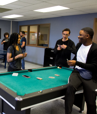 three students playing cards around a pool table